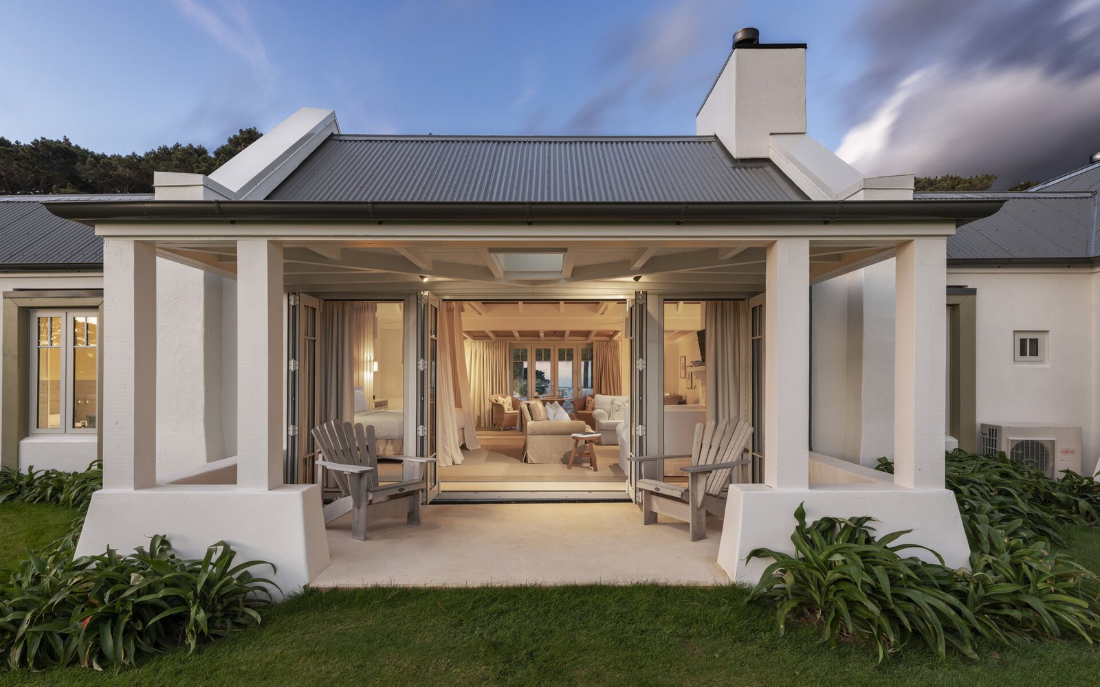 A Cottage Suite with its folding doors opened right across, two timber chairs under the veranda, light falling onto the lawn