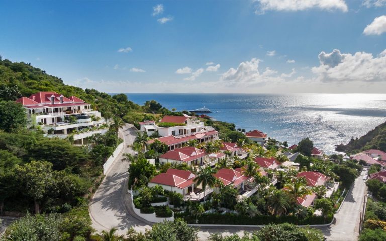 Fouquet's Saint-Barth 航拍：红屋顶小房子顺着 Gustavia 的山坡排下去，山下是海与停泊的游艇