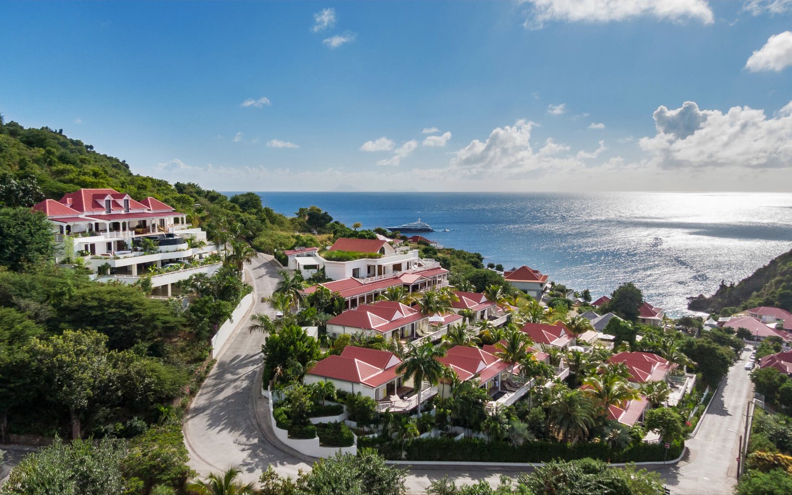 Aerial view: red-roofed cottages stepping down the hillside above Gustavia, the sea and anchored yachts below