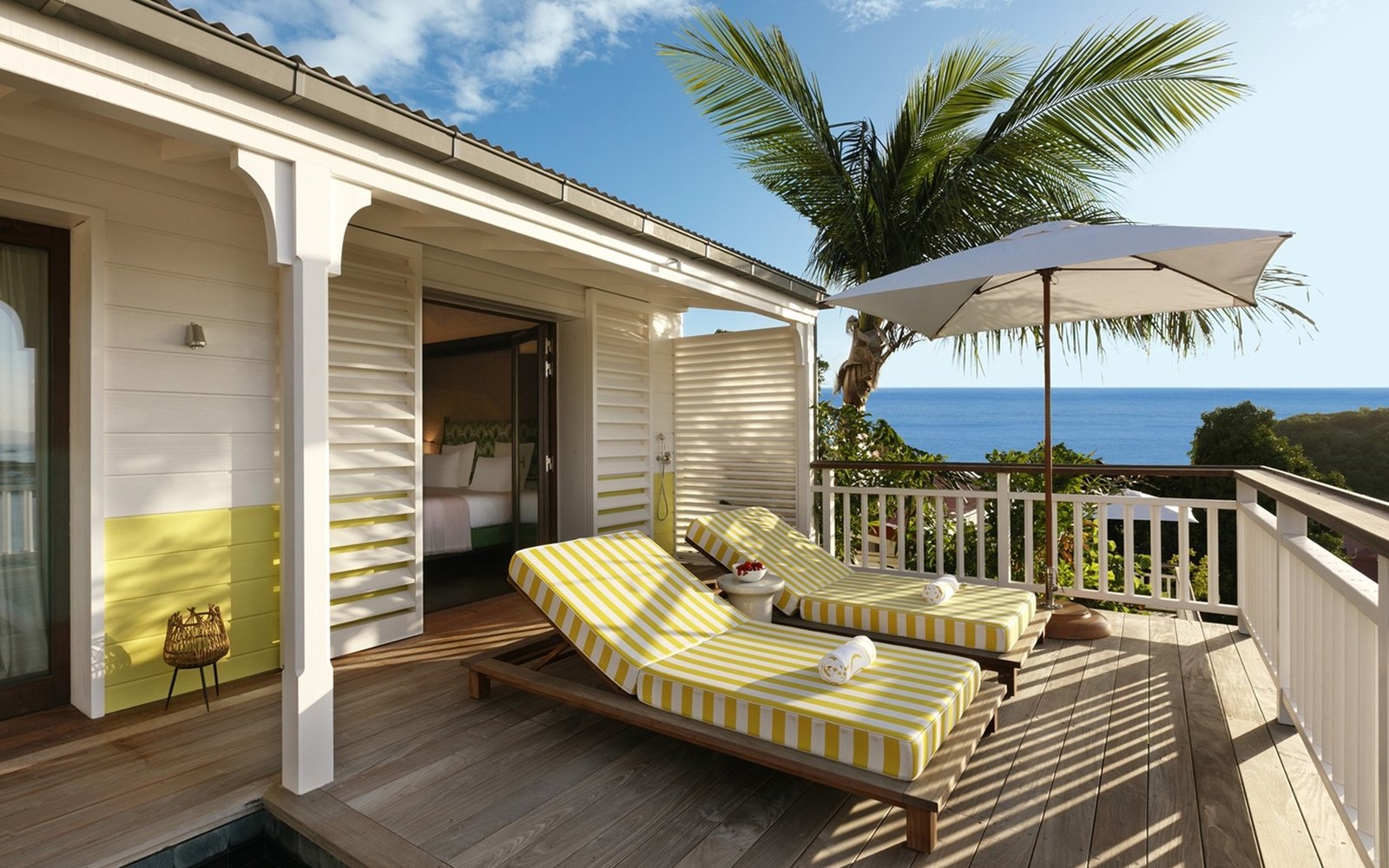 Two striped loungers and a white parasol on a timber terrace, a palm overhead, a small plunge pool at the edge